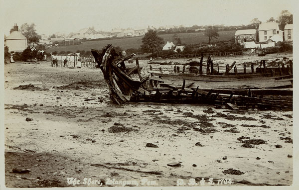Postcard of the foreshore at Llangwm Pembrokeshire with a broken boat in the foreground and several people standing on the shore